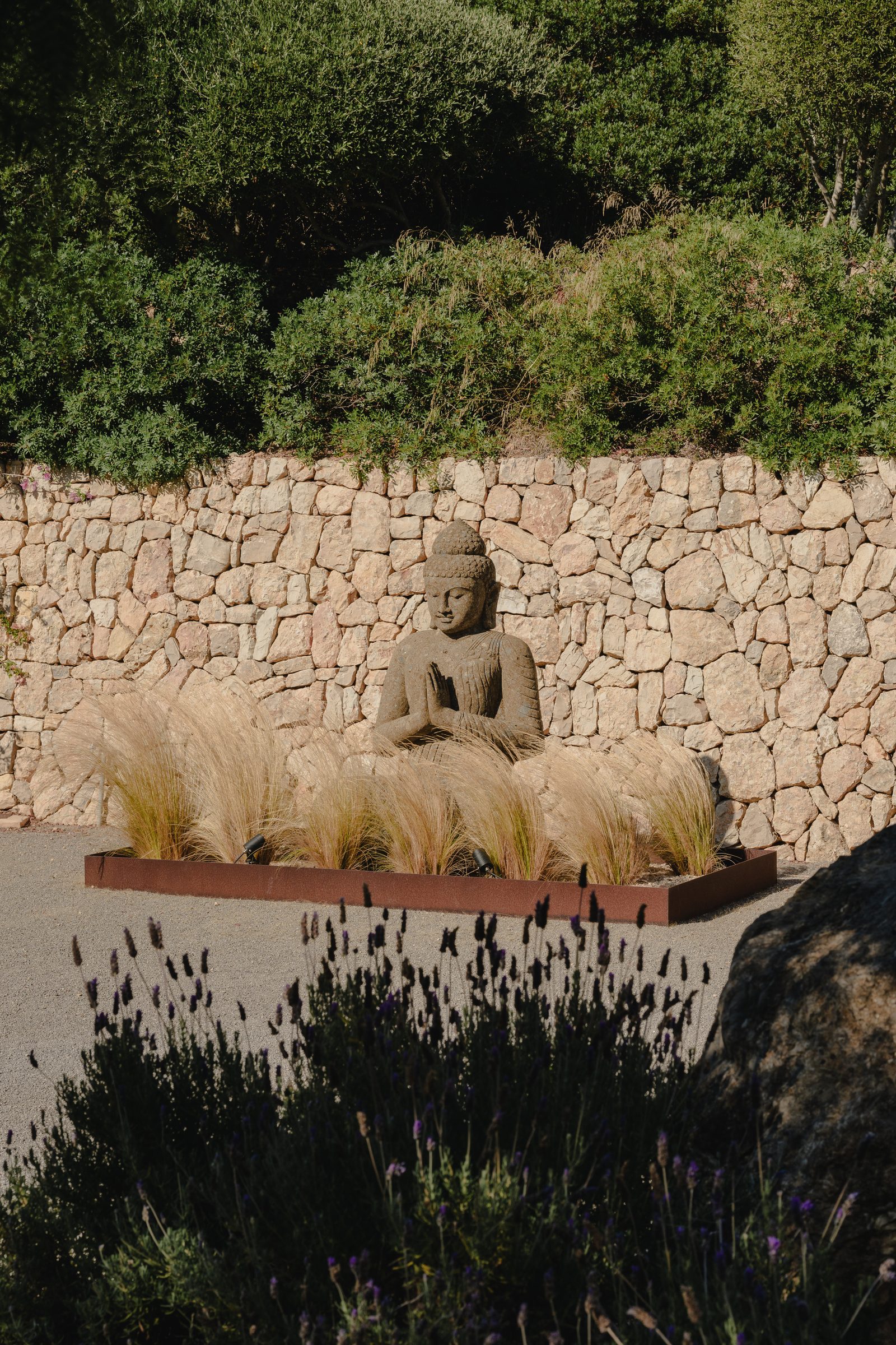 Buddha-Skulptur an der Natursteinmauer mit Gräsern und Lavendel